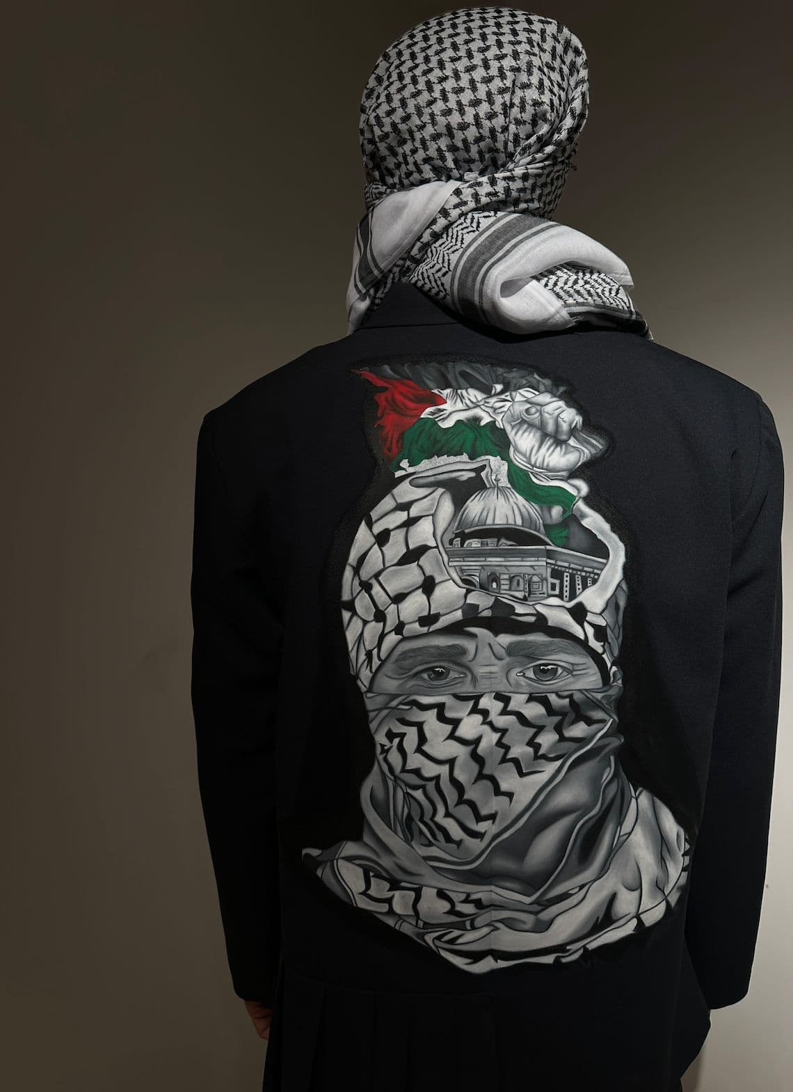 Atelier Qeblawi Painted Suit — back panel close-up showing a hand-painted figure in a kufiyeh face-wrap with the Dome of the Rock and Palestinian flag emerging from the headwrap.